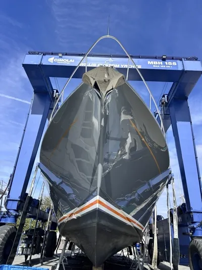 Dark racing hull under a travel lift, finished to a mirror